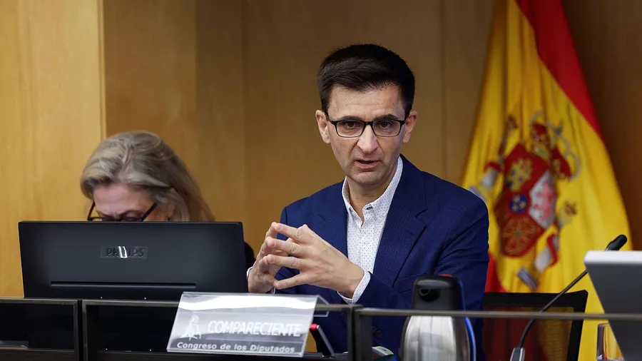 José Pablo López, presidente de RTVE, gesticulando con las manos durante una comparecencia ante la Comisión Mixta de Control Parlamentario, con la bandera de España al fondo